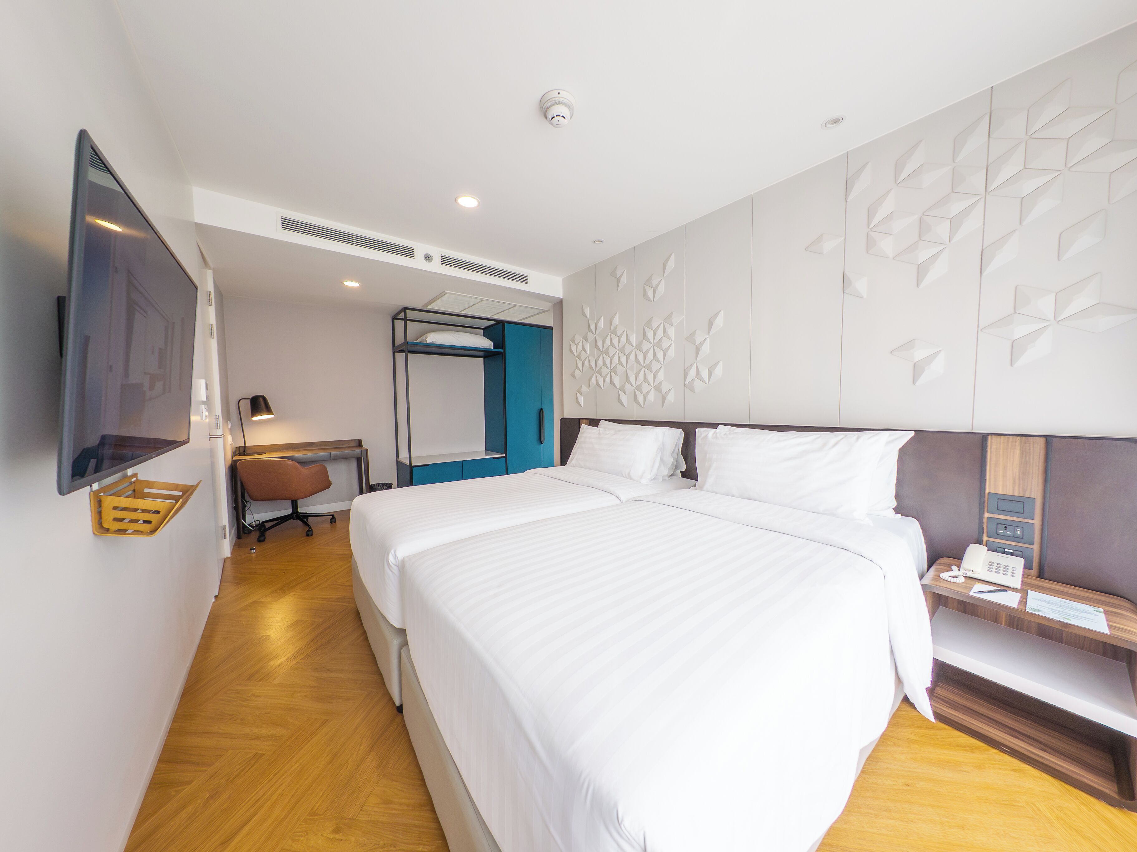 Ein modernes Hotelzimmer mit einem großen Bett, einem Schreibtisch mit Stuhl, einem flachbildfernseher an der Wand und einer dekorativen Wandverkleidung.