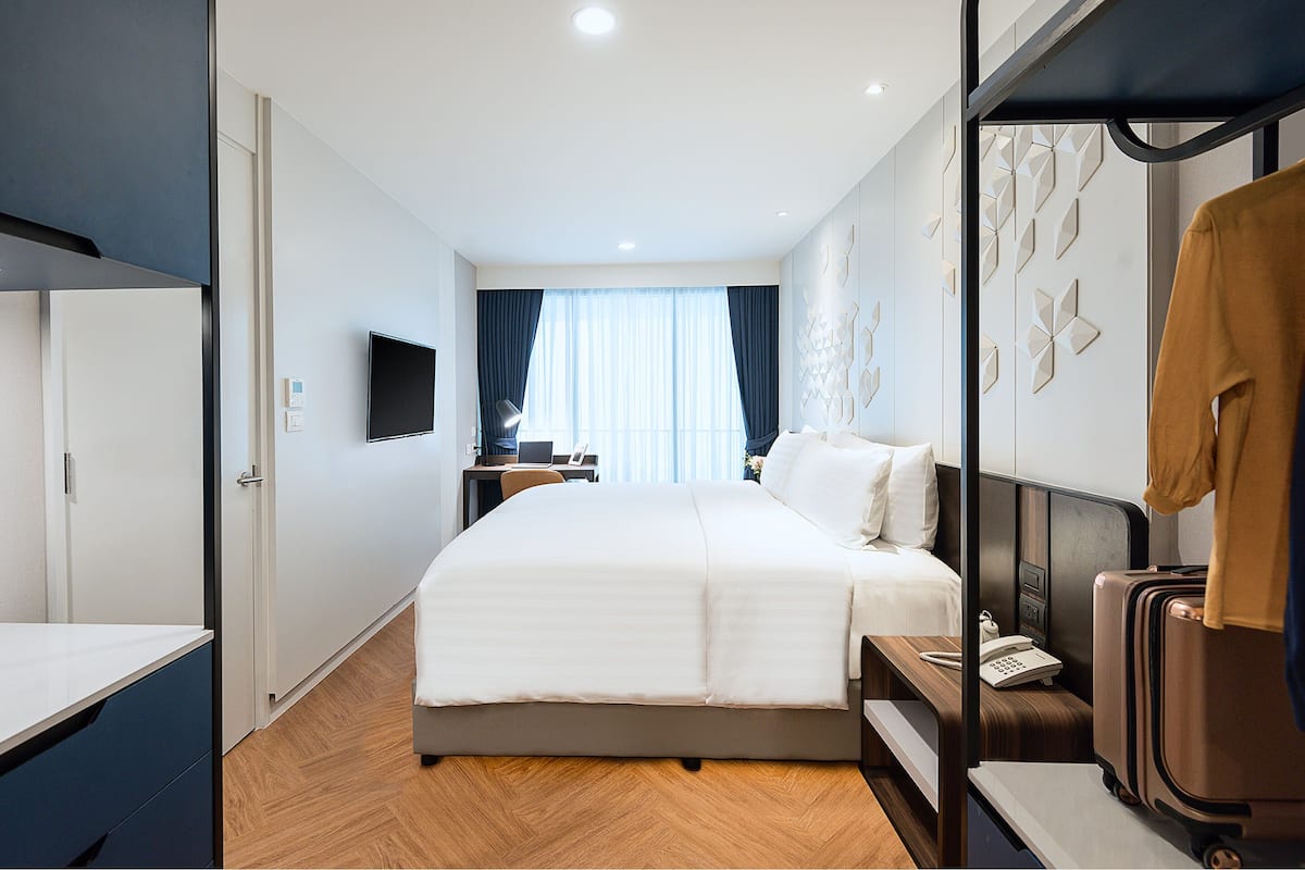 Habitación de hotel con cama, escritorio, silla, televisor y maleta.