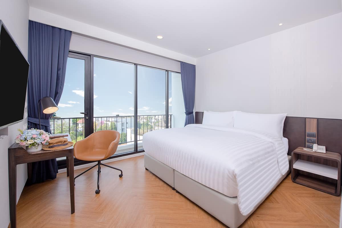 Habitación de hotel con una cama grande, un escritorio con lámpara, una silla y una mesita de noche con teléfono.