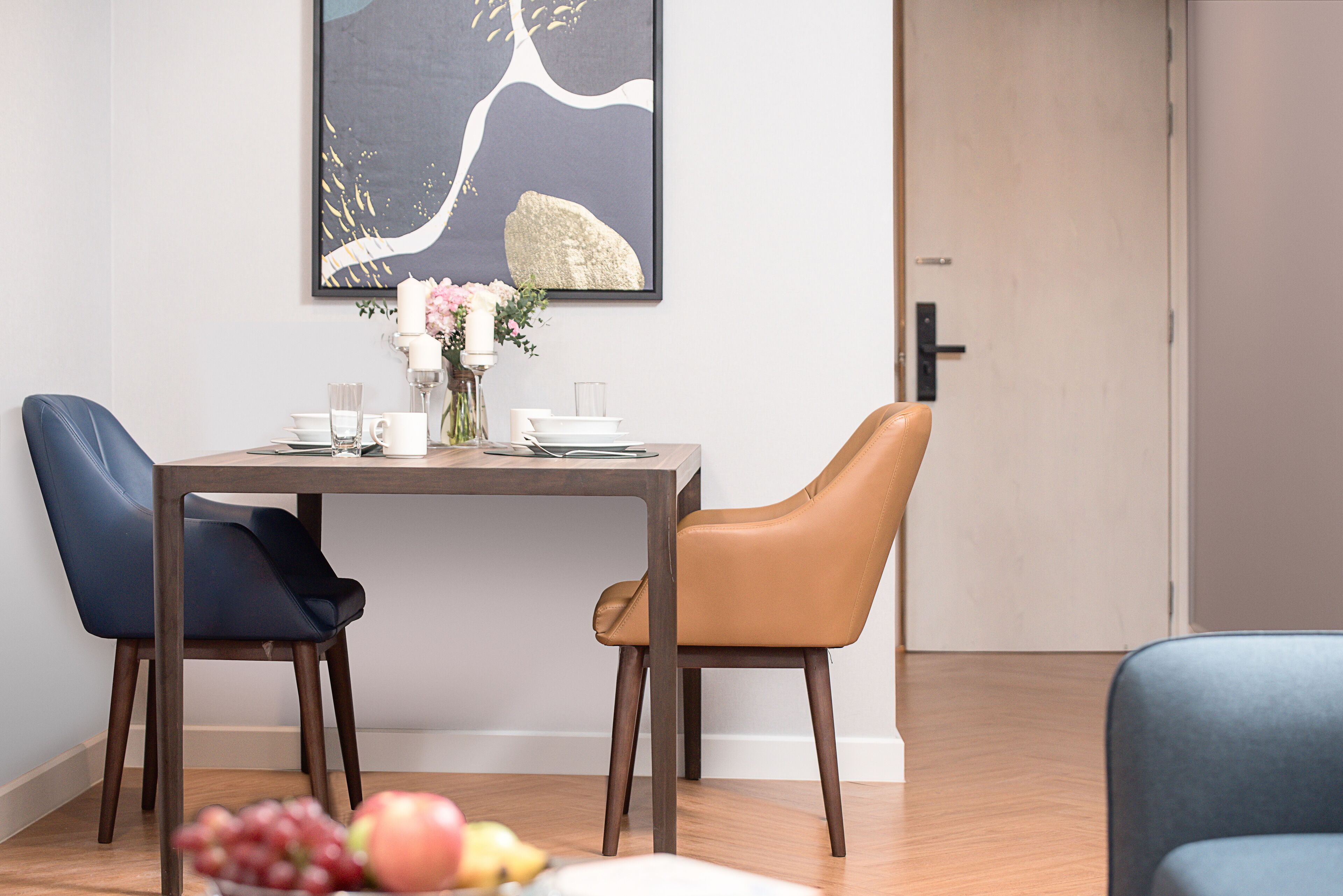 A dining area with a table set for two, a vase with flowers, and a fruit bowl on the table.