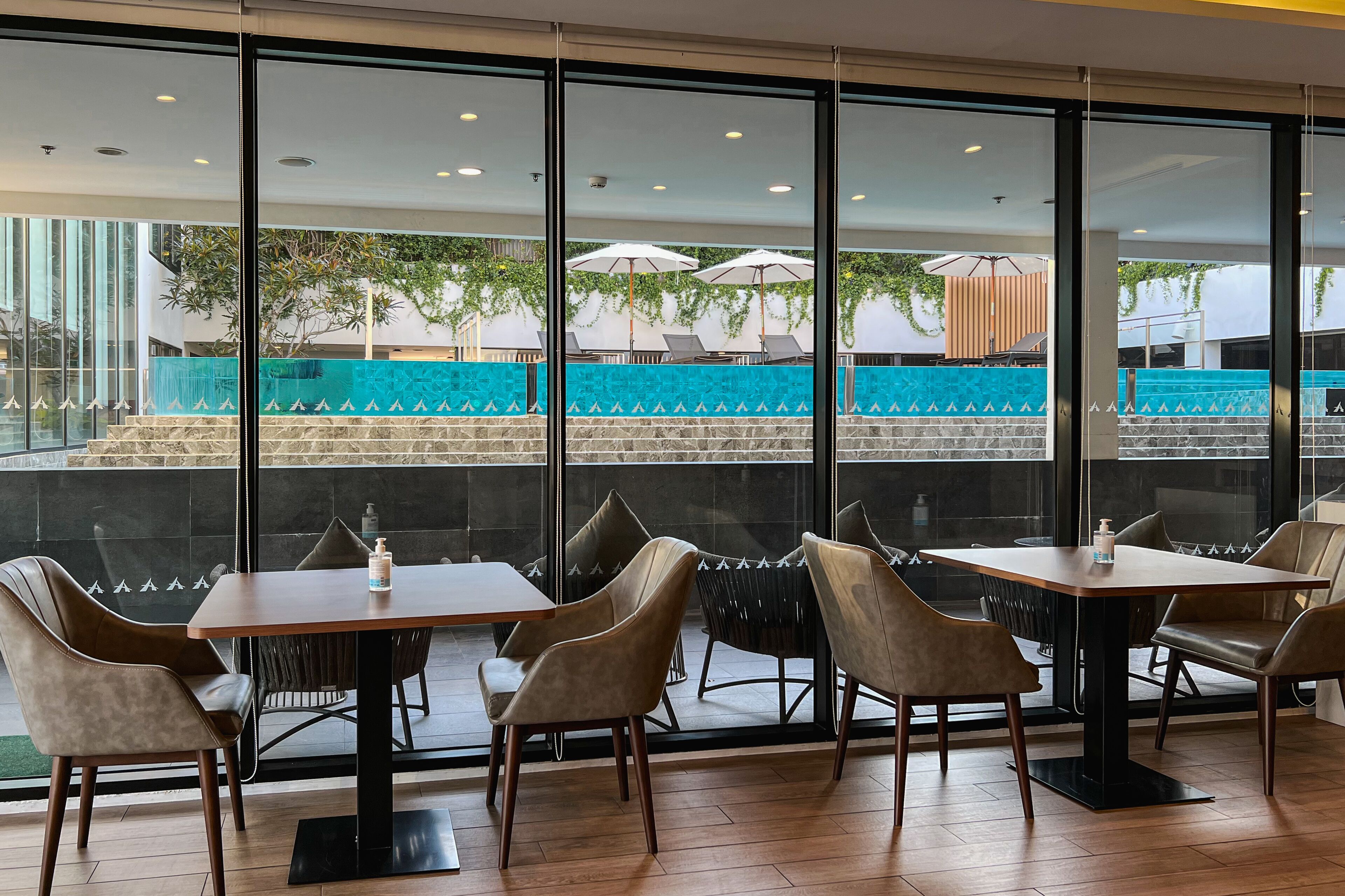 A modern indoor dining area with large windows, a pool view, and a mix of leather and fabric chairs.