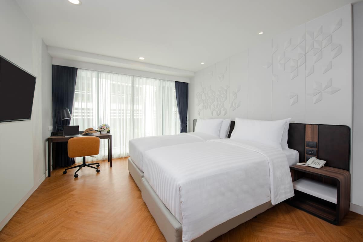 Una habitación de hotel moderna con una cama grande, un escritorio con una computadora portátil y un teléfono en una mesita de noche.