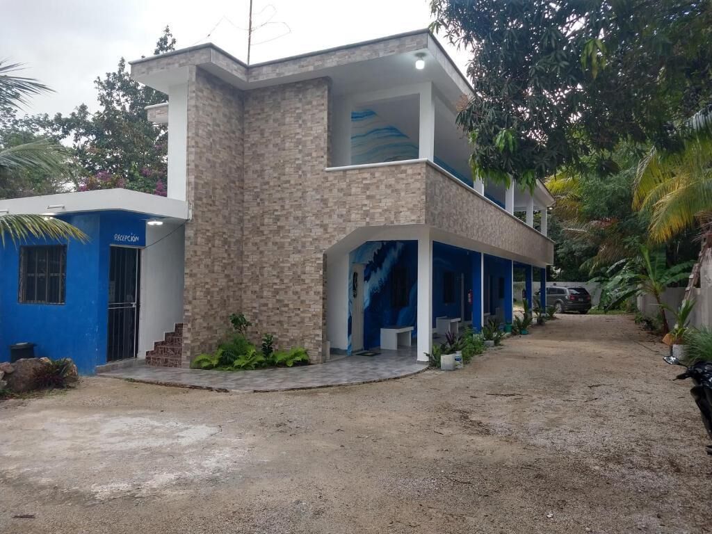 Un edificio de dos plantas con fachada azul y beige, un espacio al aire libre cubierto con asientos y un camino de entrada de grava.