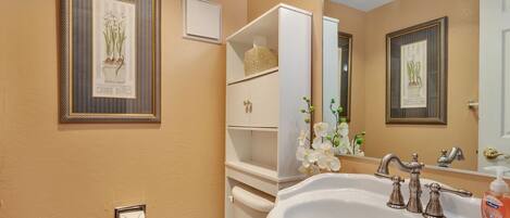 A bathroom with a toilet, sink, and shelves with toiletries.