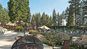 Uma área de estar externa com lareira, cadeiras e vista para uma piscina e área arborizada.