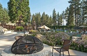 An outdoor seating area with a fire pit, chairs, and a view of a pool and forested area.