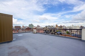 A rooftop terrace with a view of a cityscape, featuring a metal railing and a concrete floor. - Hostel Coliberty (Tokushima)