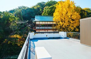 A traditional Japanese building with a sloped roof, surrounded by lush greenery and autumn-colored trees. - Hostel Coliberty (Tokushima)