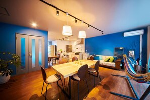 A modern living space with a dining area, kitchen, and a hammock. - Hostel Coliberty (Tokushima)