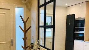 Una cocina moderna con una mesa de vidrio, un perchero de madera y un refrigerador negro.