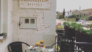 Un patio con mesa y sillas, un letrero que dice "HACIENDA MONTORIO" y vistas de la calle y la vegetación.