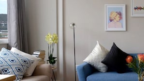 Ein Wohnzimmer mit einem blauen Sofa, weißen und gemusterten Kissen, einer Vase mit Blumen und gerahmten Kunstwerken an der Wand.