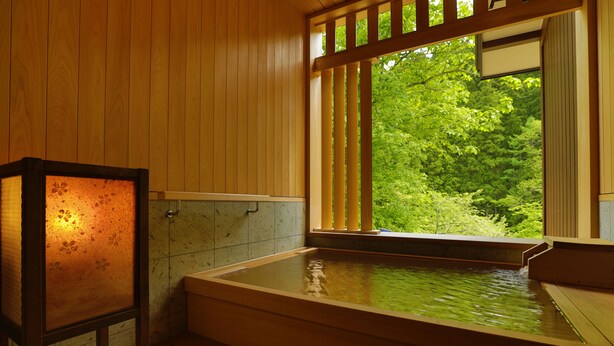 A traditional Japanese onsen with a wooden interior, a stone wall, and a view of lush greenery outside. - Yukemuri no yado Inazumi onsen (Yuzawa)