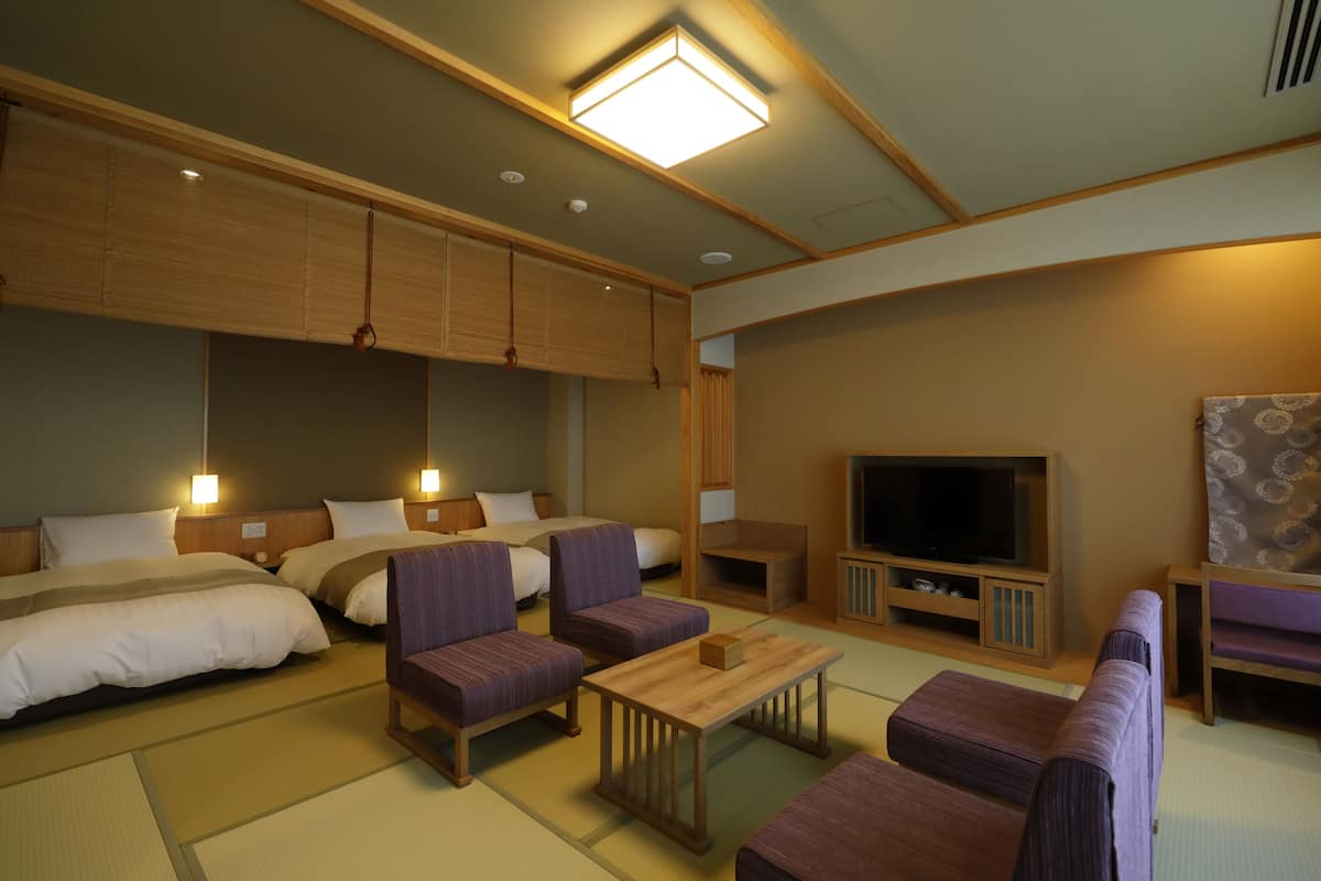 A hotel room with two beds, a sofa, a TV, and a wooden cabinet.