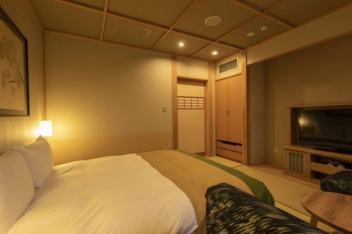 A hotel room with a bed, a television, a wooden wardrobe, and a small table.