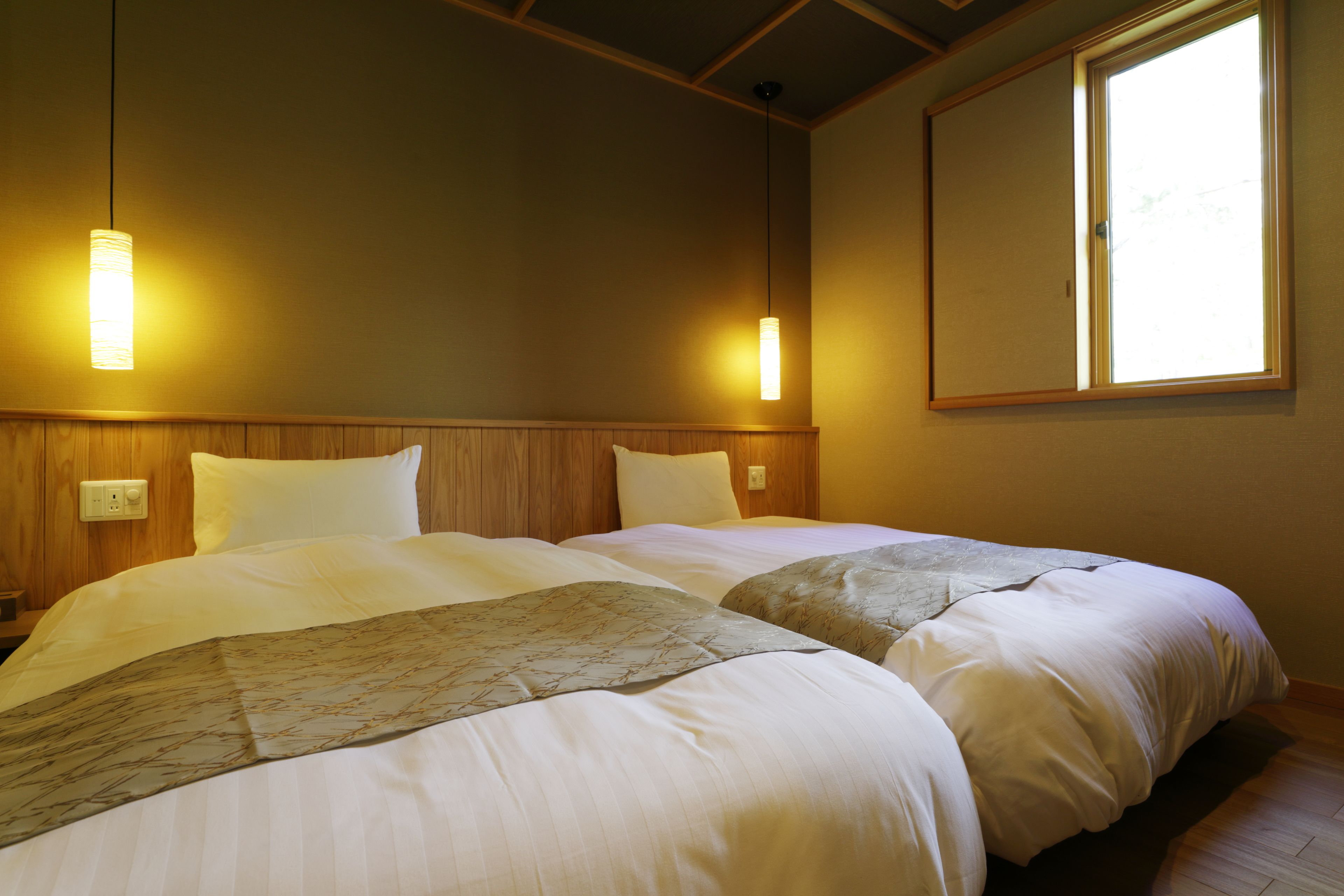 A hotel room with two beds, wooden headboard, bedside lamps, and a large window.