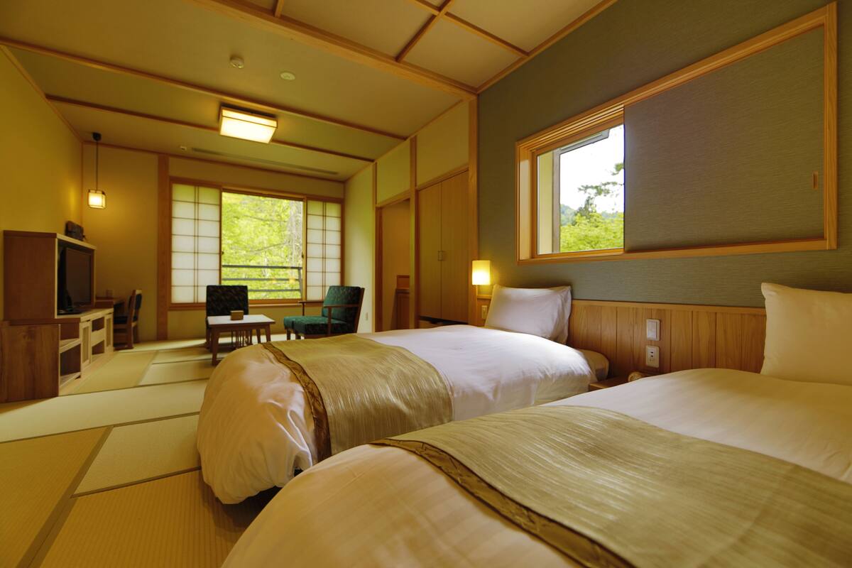 A traditional Japanese-style hotel room with tatami flooring, two beds, a desk, and a television.