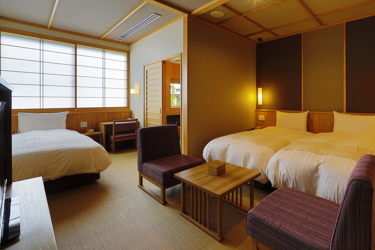 A hotel room with two beds, a desk, a chair, and a small table.
