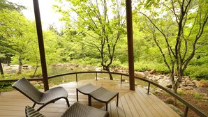 A wooden deck with wicker furniture overlooking a natural landscape with trees and a stream. - Yukemuri no yado Inazumi onsen (Yuzawa)