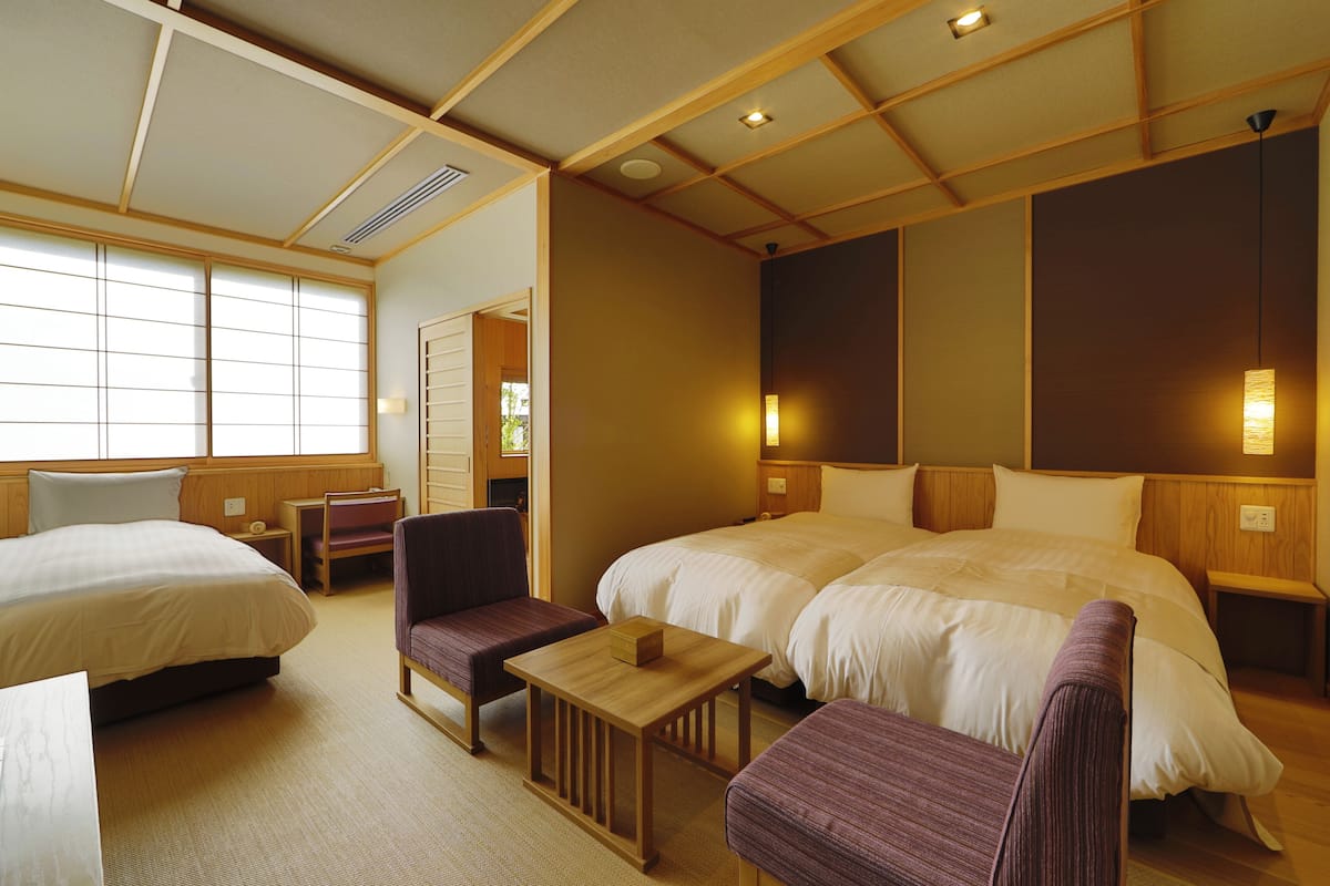 A hotel room with two beds, a small table, a chair, and a desk.