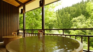 A hot tub with a wooden deck and a view of a forested area. - Yukemuri no yado Inazumi onsen (Yuzawa)