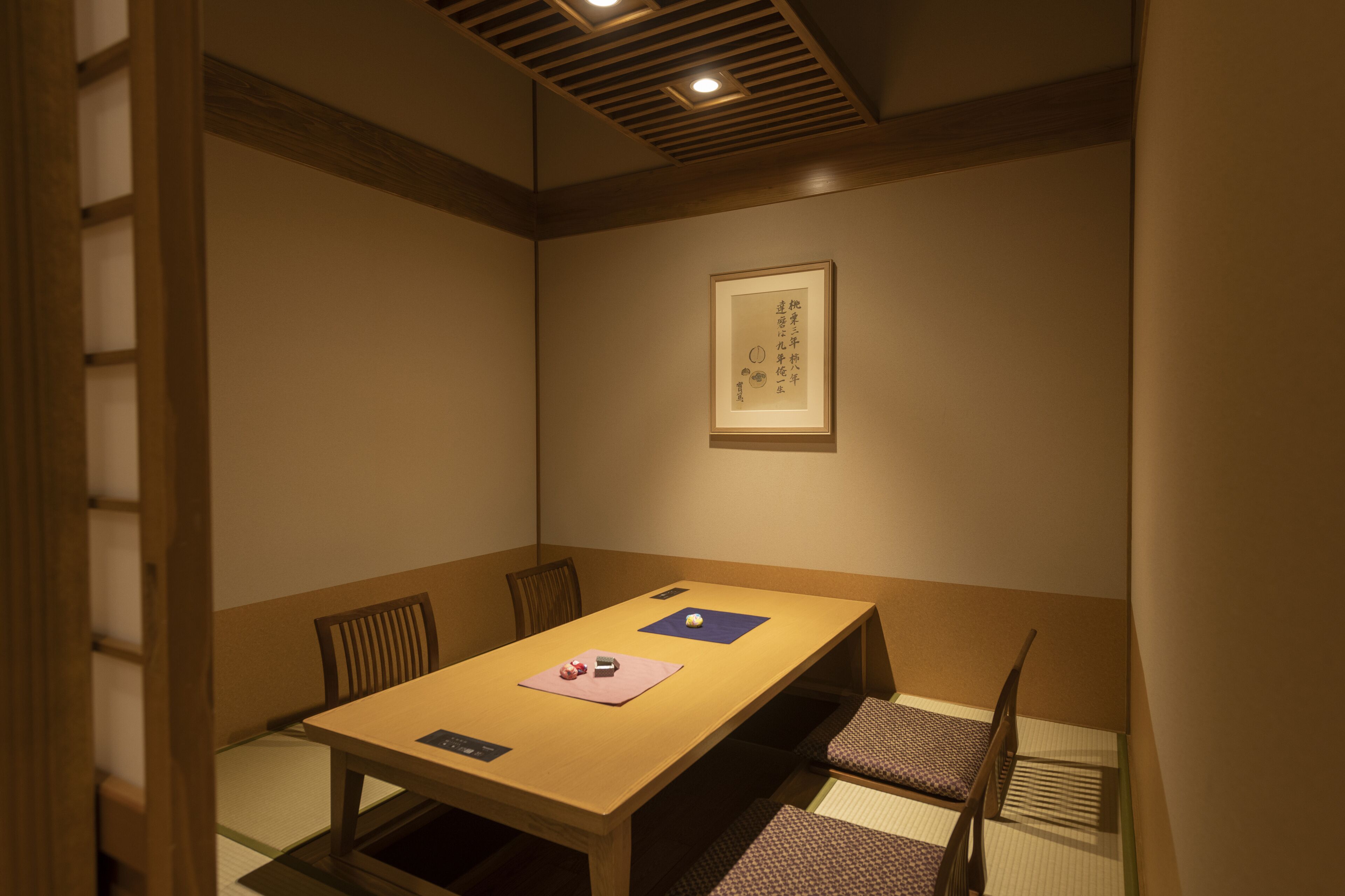 A traditional Japanese-style room with tatami flooring, a low wooden table, and a framed calligraphy piece on the wall.