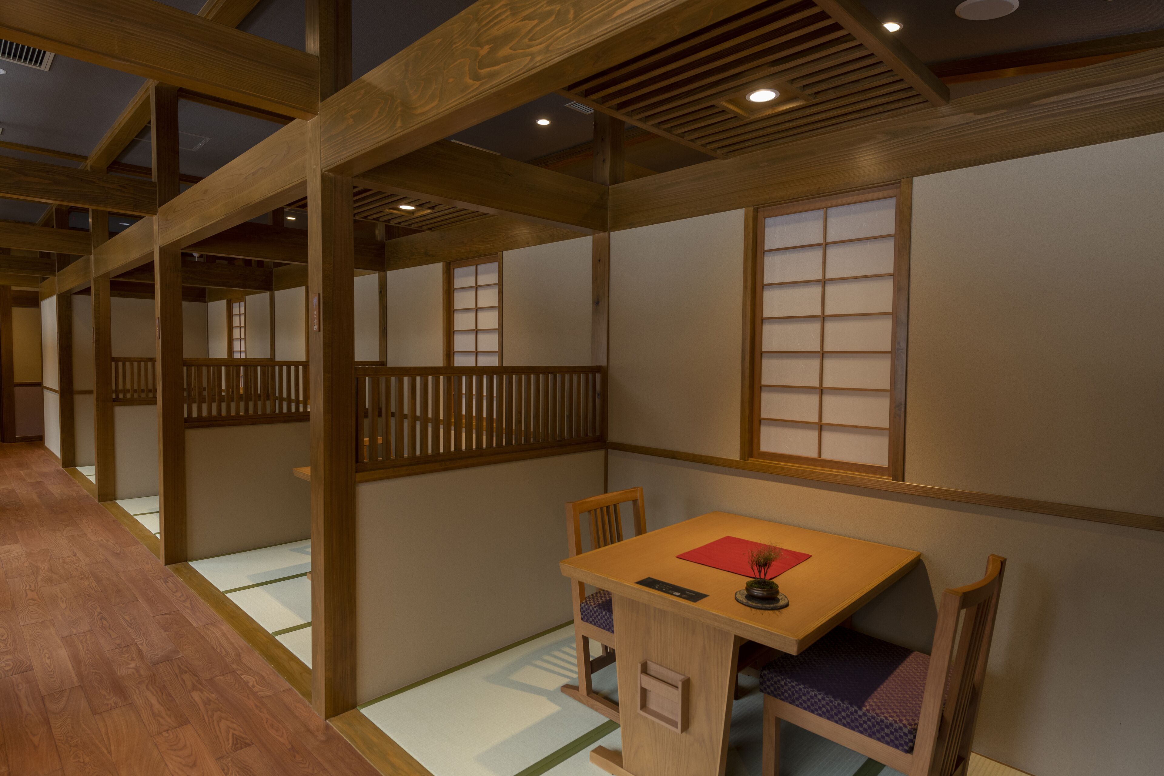 A traditional Japanese-style room with tatami flooring, wooden beams, sliding doors, and a low wooden table with a cushion.