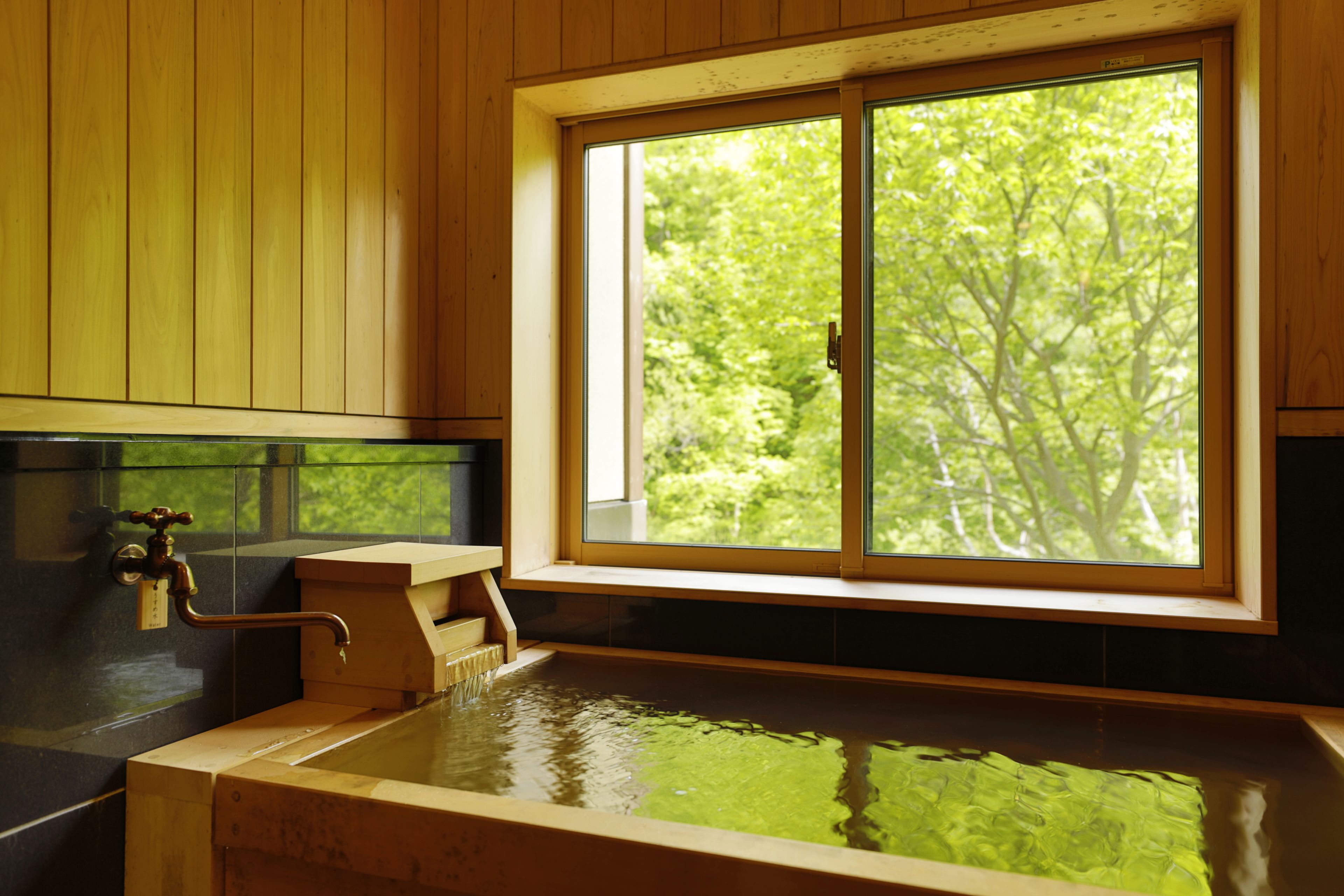 A wooden cabin with a large window, a wooden bathtub, and a faucet.