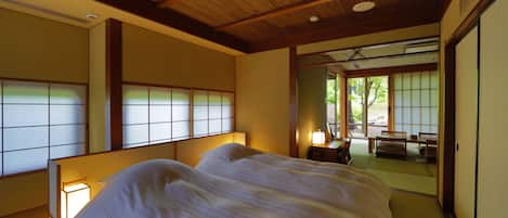 A traditional Japanese-style room with tatami flooring, a large bed, sliding shoji doors, and a view of a garden.
