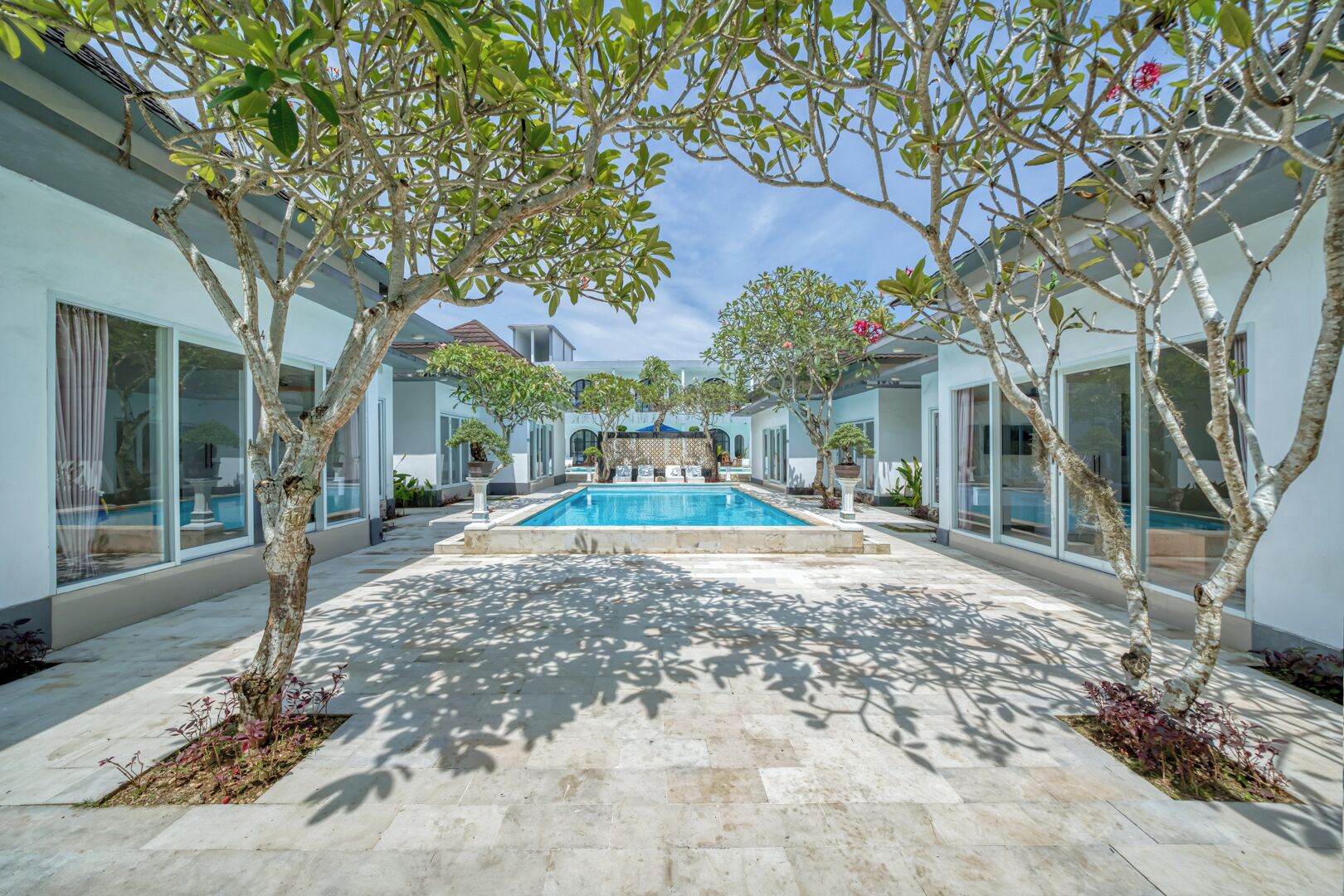 A pool area with a clear view of the pool, surrounded by trees and a modern building with large windows.