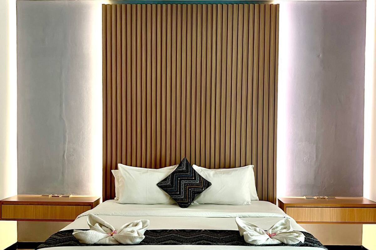 A modern hotel room with a large bed, wooden headboard, and bedside tables.