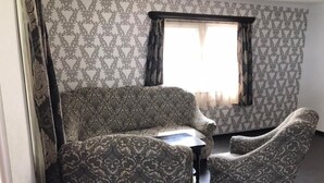 Ein Zimmer mit gestreiftem Wandteppich, einem Fenster mit Vorhängen und zwei Sesseln.