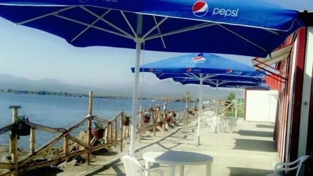 Ein Restaurant am Meer mit Terrassenplätzen, blauen Sonnenschirmen und Blick auf das Wasser.