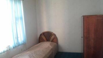 Ein kleines Zimmer mit einem Einzelbett, einem Holzkopfende, einem Kleiderschrank und einem Fenster mit Jalousien.