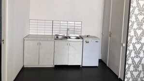 Eine kleine Küche mit weißer Arbeitsplatte, zwei Spülen, einem Kühlschrank und einer gefliesten Rückwand.