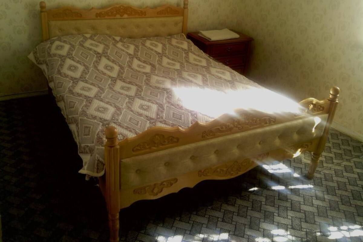 Una cama con colcha estampada, cabecera de madera y mesita de noche con lámpara.
