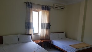 A room with two beds, a window with curtains, an air conditioning unit, and a small table. - CatBa-Withlocals (Hai Phong)