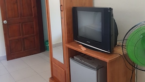 Una habitación con un armario de madera, televisión, refrigerador pequeño y ventilador.