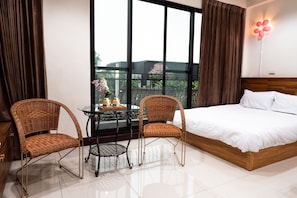 A hotel room with a large bed, two wicker chairs, a small table with a vase, and a view of greenery through large windows. - Happy Holiday Homestay (Shuishang)