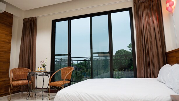 A hotel room with a large bed, two wicker chairs, a small table with a vase, and a balcony with a view of greenery. - Happy Holiday Homestay (Shuishang)