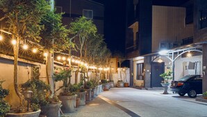 A nighttime street scene with a row of potted plants and string lights along a sidewalk, leading to a building with a car parked in front. - Happy Holiday Homestay (Shuishang)