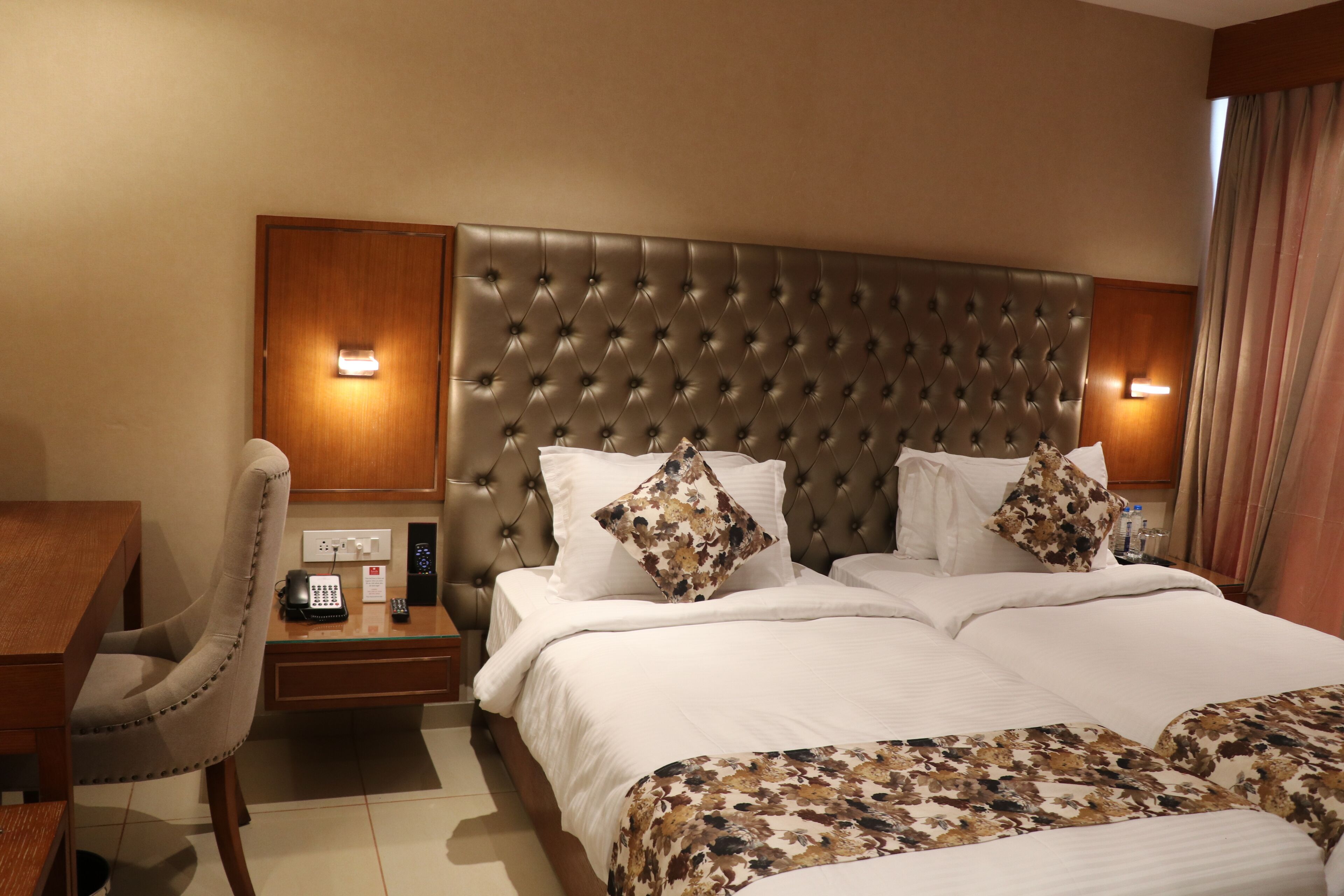 Ein Hotelzimmer mit einer karottenförmigen Kopfteil, einem Schreibtisch mit Telefon und einem Bett mit blumigem Bettbezug.