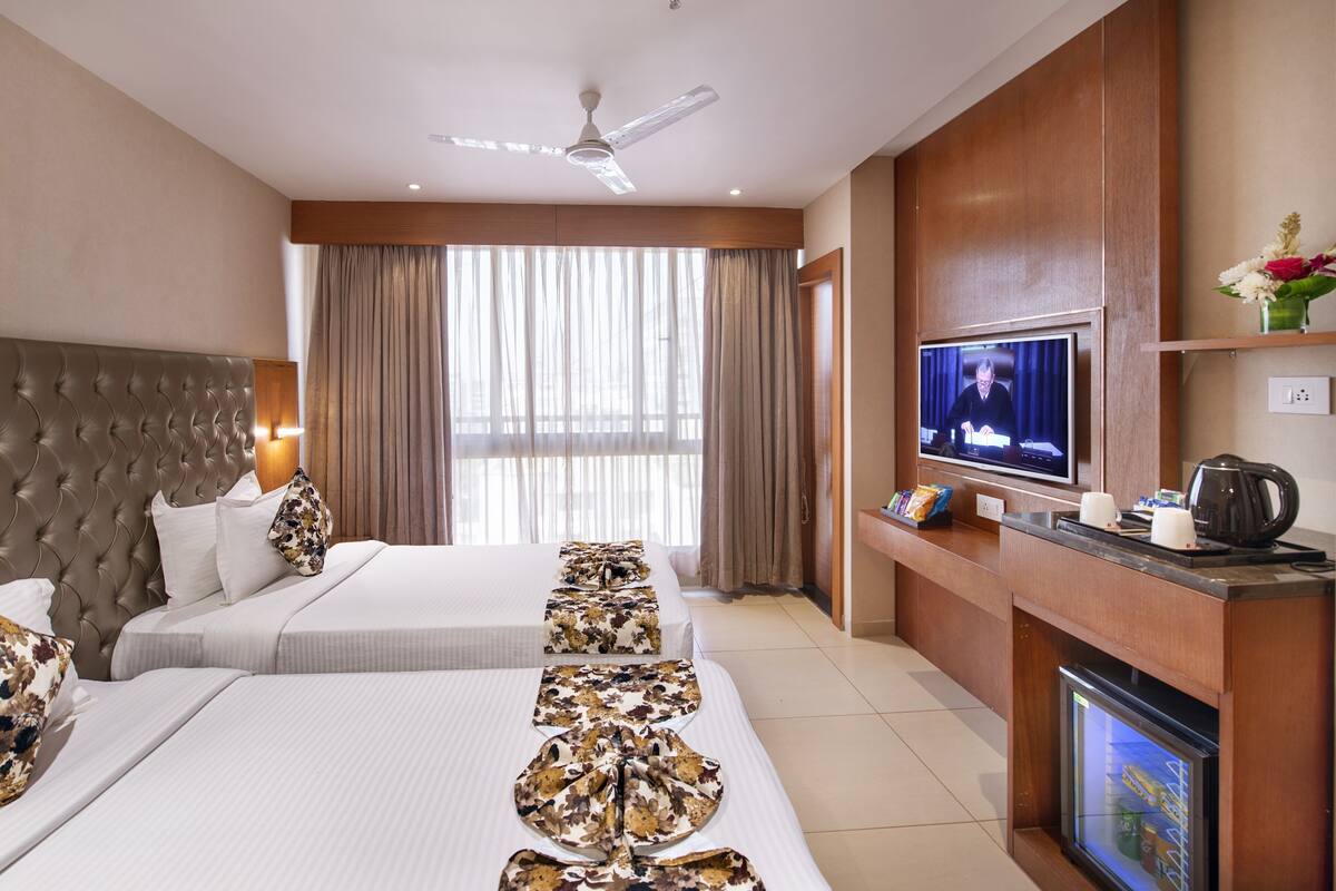 A hotel room with a large bed, a smaller bed, a TV, a coffee maker, and a fireplace.