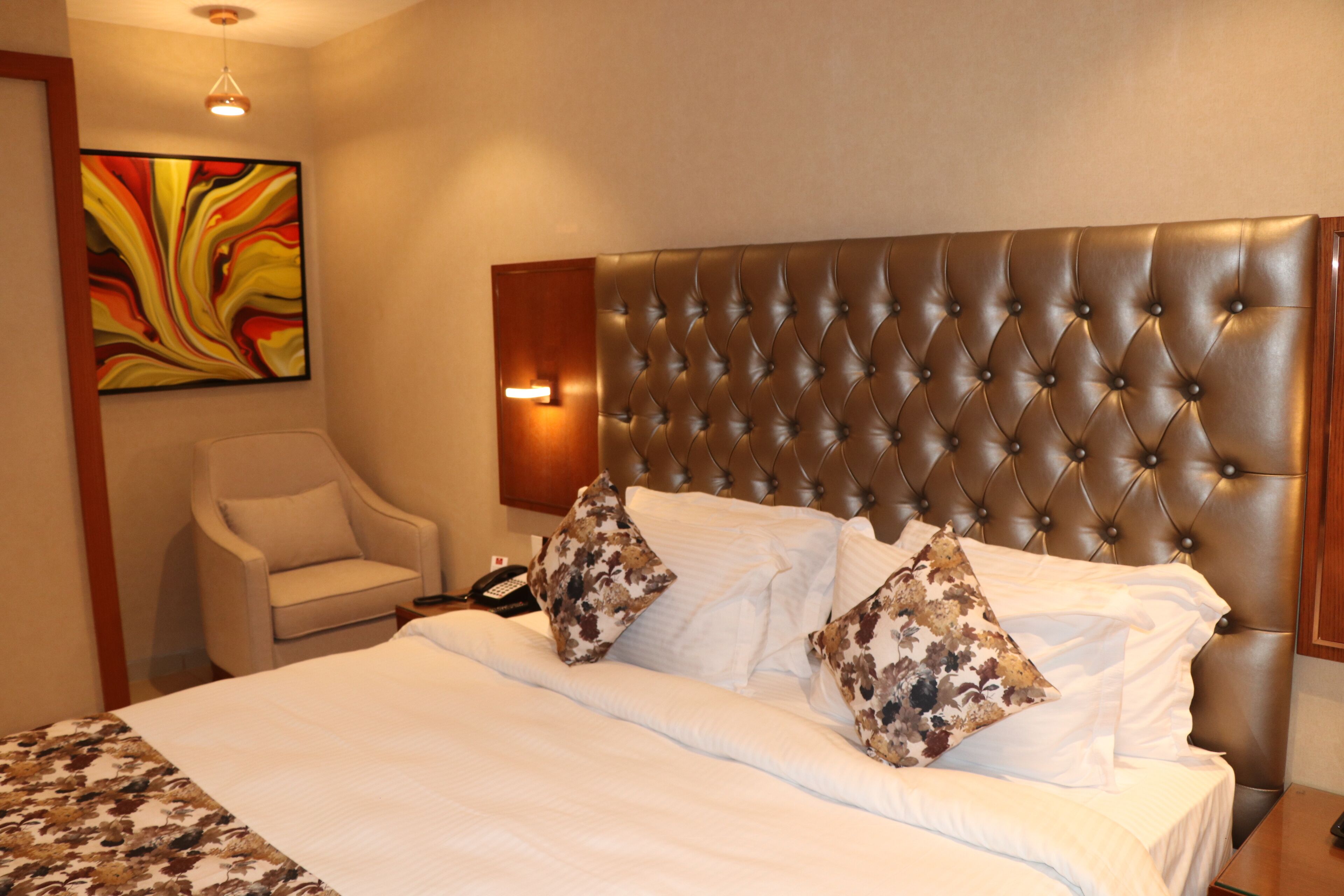 A hotel room with a large bed, a tufted headboard, a chair, and a painting on the wall.