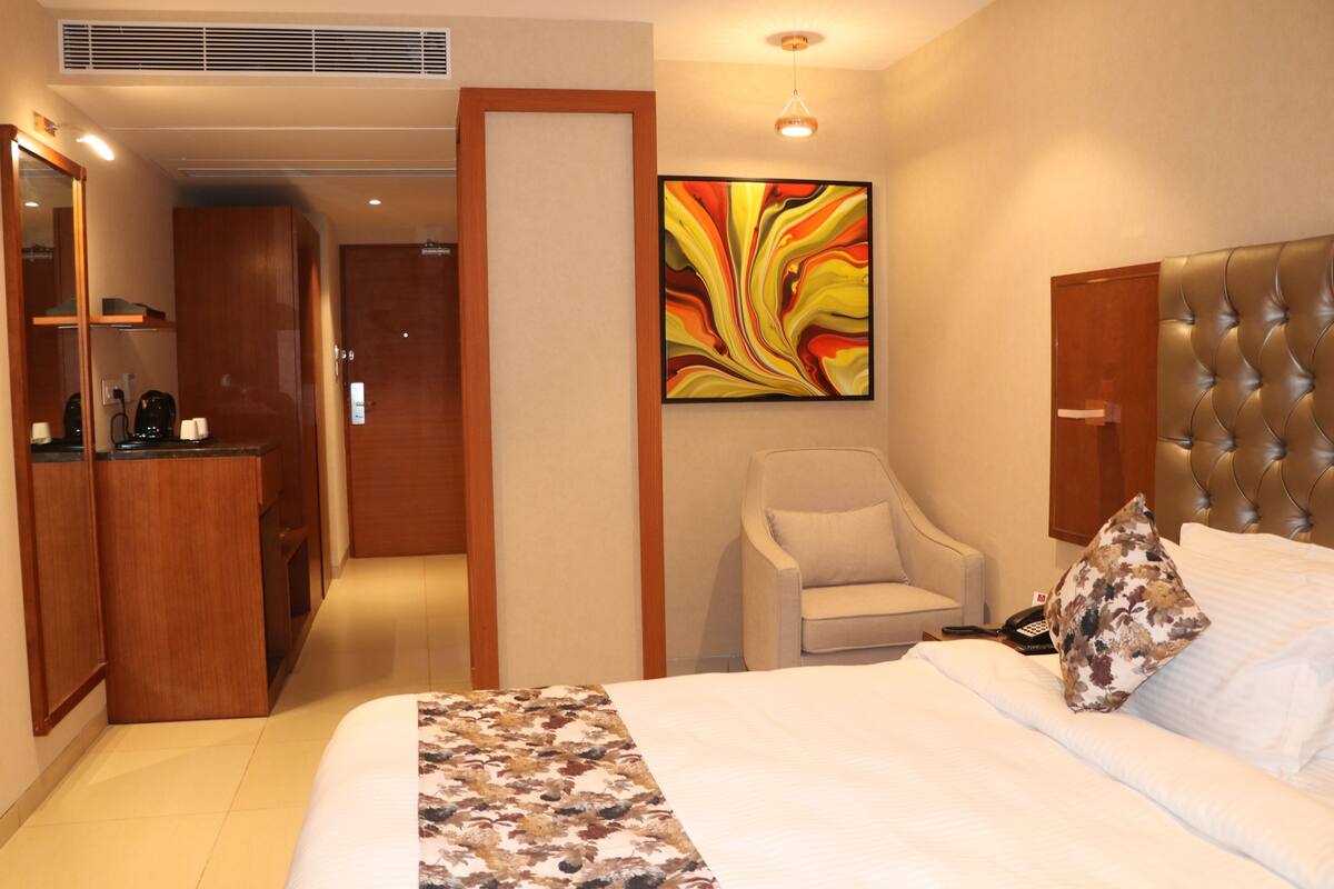 A hotel room with a bed, a chair, a desk, and a painting on the wall.
