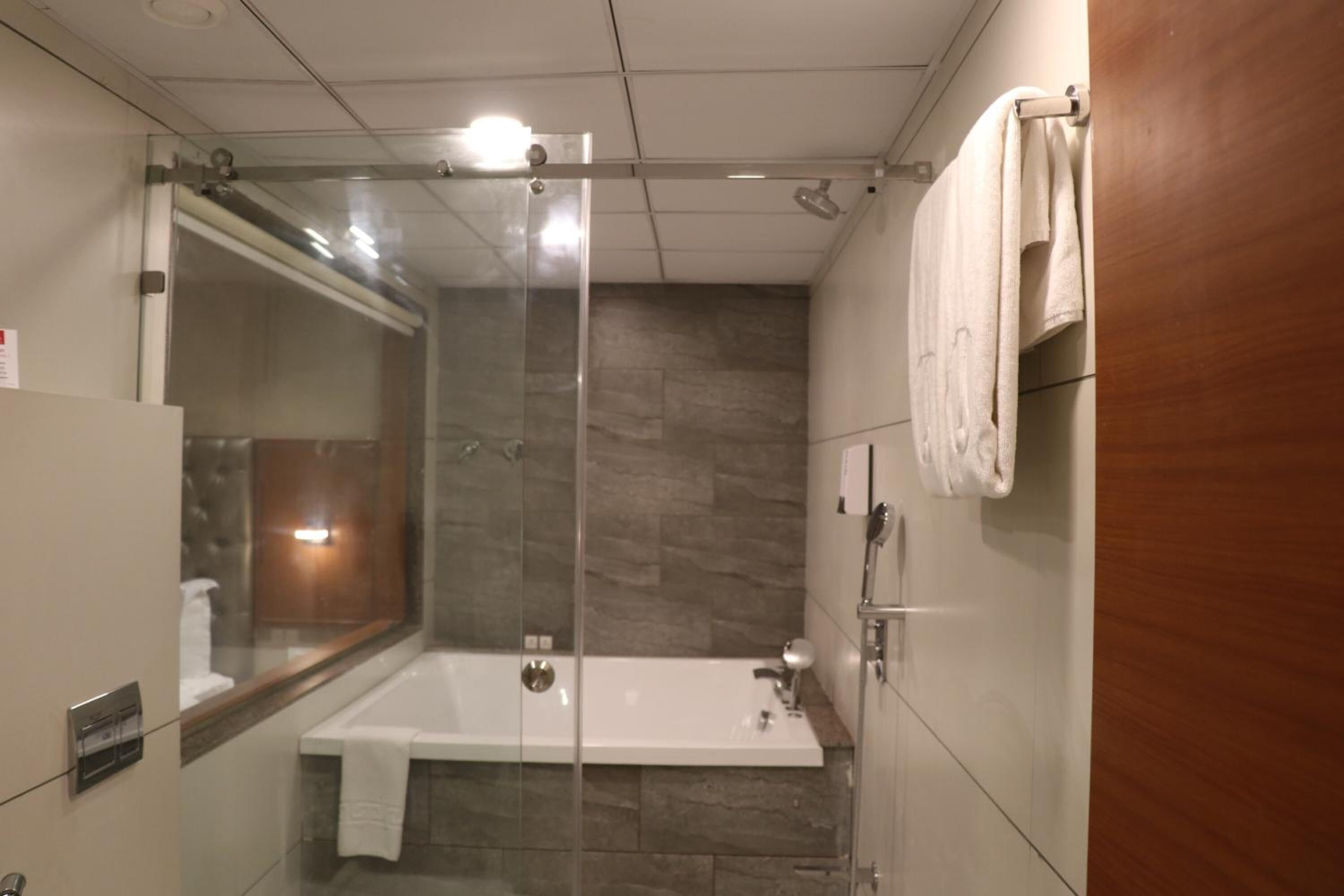 A modern bathroom with a glass-enclosed shower, a white bathtub, and a wooden vanity.