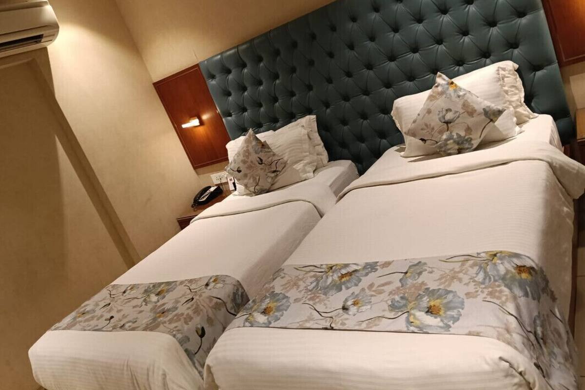 A hotel room with a large bed, a tufted headboard, floral-patterned bedding, and a bedside telephone.