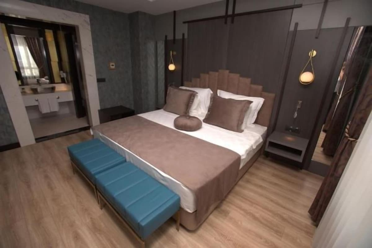 Un dormitorio moderno con una cama grande, un banco, un espejo y un armario.