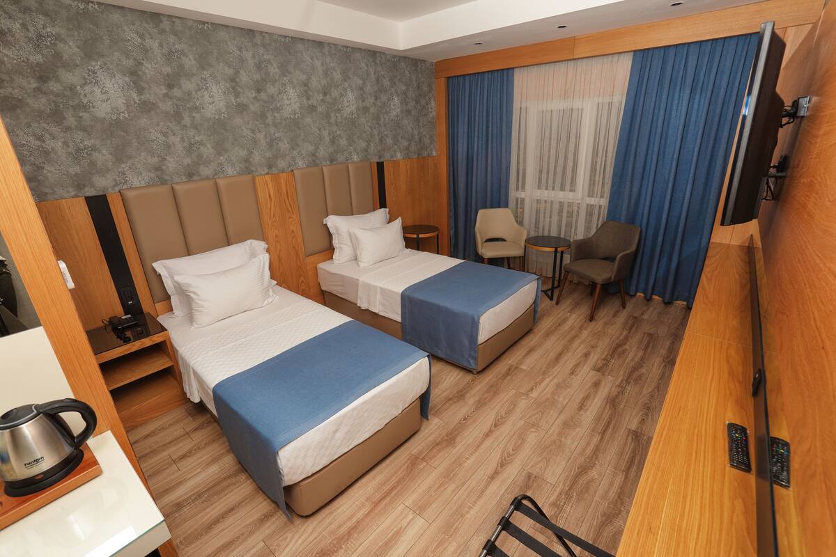 A hotel room with two beds, a desk, a chair, a TV, and a window with curtains.