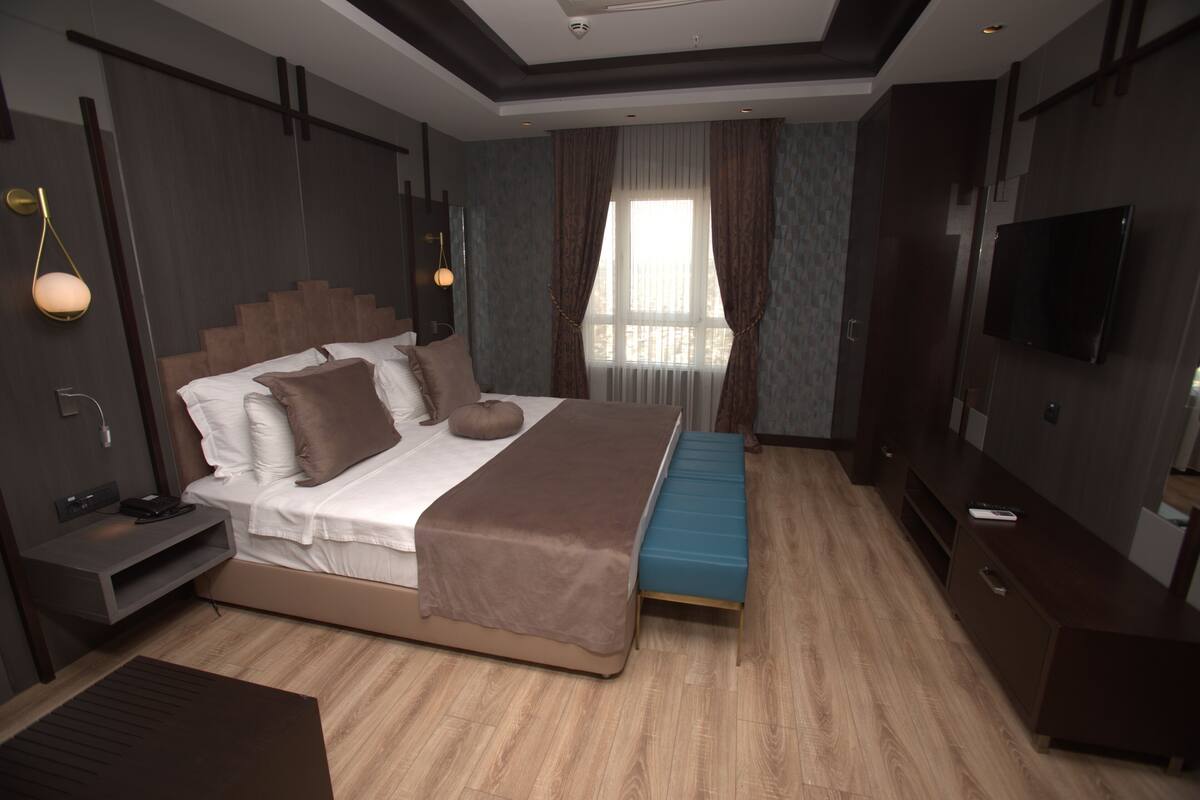 A modern hotel room with a large bed, a bench, a TV, and a desk with a lamp.
